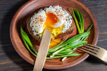 Delicious sandwich with bread, salad of green wild garlic, soft-boiled egg and sour cream on plate, closeup