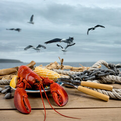 Lobsters on a plate on a seaside dock with driftwood and ropes and lobster fishing boats in the...