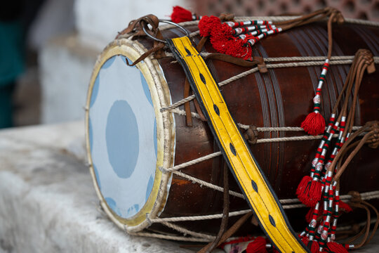 Traditional drum or dhol instrument with yellow band and red flowers placed on the floor. 