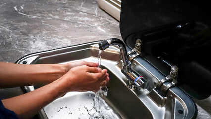 Washing the hands in the sink under the tap with clean water, modern kitchen interior style of the...