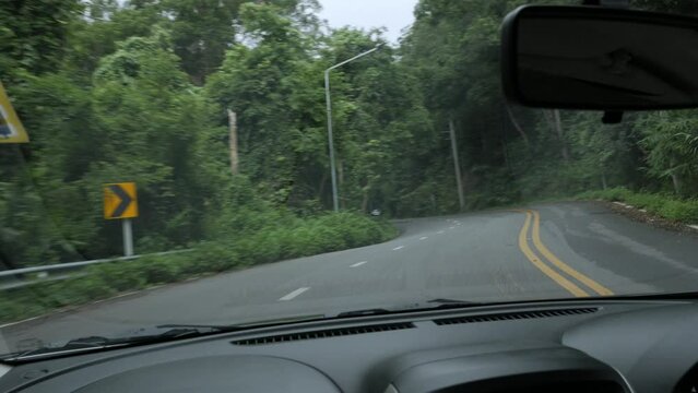 view of the country side road from inside car while moving through the rain forest on the mountain in northern area of Thailand from front camera