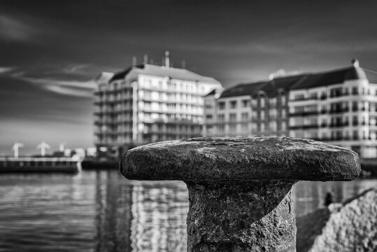 A CITY BY THE SEA - Old rusty bollard on the port quay and a holiday resort in the background
