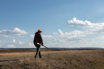 Mature man hunter with gun while walking on field.