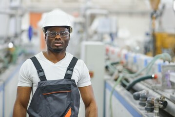 Portrait of industrial engineer. Smiling factory worker with hard hat standing in factory...