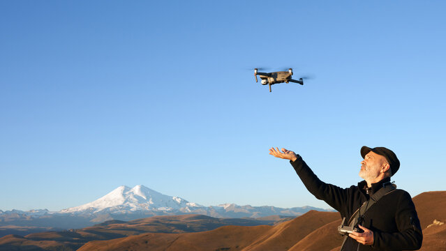 Landscape aerial photography at dawn. An adult man puts a quadrocopter on his arm. A picturesque mountain landscape with snow-covered Elbrus in the background. Copy space.