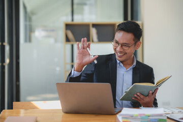 Smiling asian businessman with a notebook giving an online presentation. Professional webinar and virtual meeting concept.