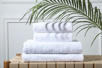 Stacked terry towels and green leaf on wicker bench indoors