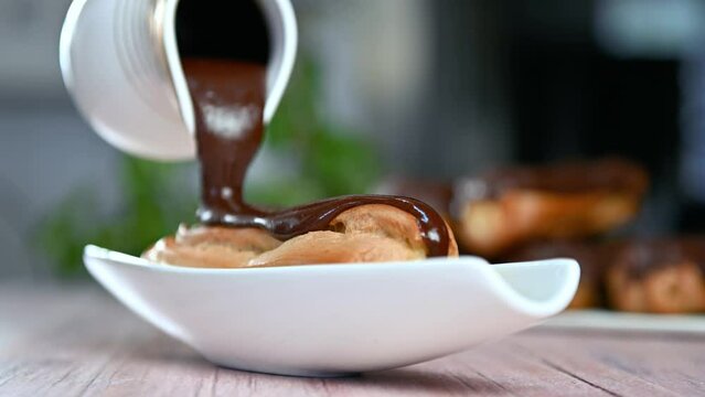 Chef coats the eclair with chocolate cream glaze. Freshly baked crispy eclairs.