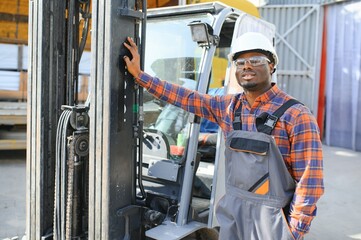 Portrait of a happy African American male worker driving forklift at workplace