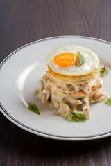 Fried eggs with pancakes in a high stack on a white plate