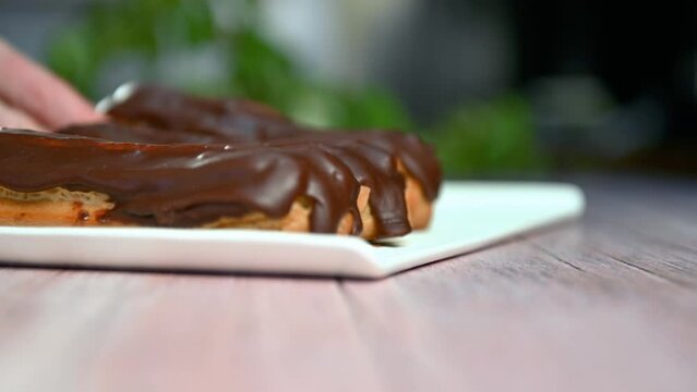 French dessert eclair with dark chocolate glaze. Woman putting baked French eclairs on a plate.