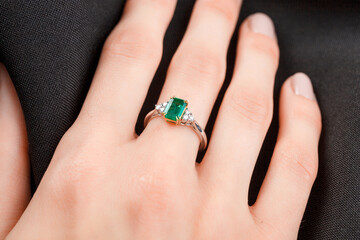 Beautiful female hand with gold ring with diamonds and emerald on gray background