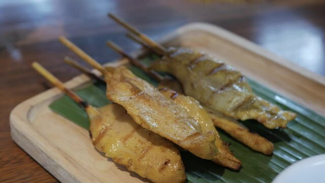 hand grabing satay skewer bbq chicken on a plate in traditional singaporean or malaysian style in traditional cruisine for appetizer