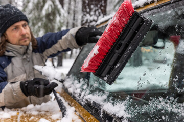 A man is cleaning his car's windshield with a brush