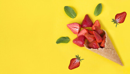 Ice cream cone with strawberry on the yellow background. Copy space. Top view.