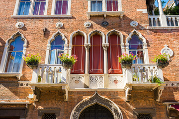 Facade of old building with typical Venetian windows and white balcony with flower pots. Venice, Italy - 752469198