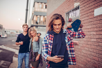 Young man with skateboard checking phone with friends in background
