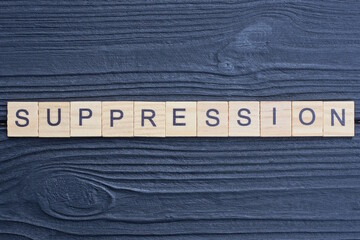 text the word suppression from brown wooden small letters on a black table
