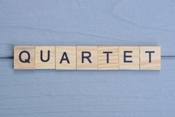 text the word quartet from brown wooden small letters with black font on an gray table