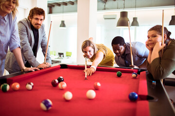 Diverse young people playing billiard in the office
