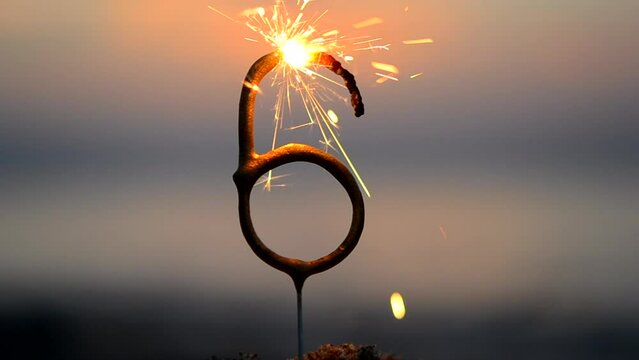 Sparkler in shape of number six 6 burning against backdrop of sea waves at dusk. Bengal fire in shape of number six 6 sparkling near sea at dawn and sunset. Concept holiday Birthday anniversary