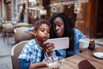 Smiling mother sitting in public cafe with son taking selfie