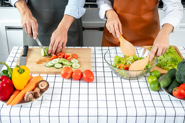 Asian romantic couple slice cucumber and tomato with knife on chopping board and holding ladle to mixing