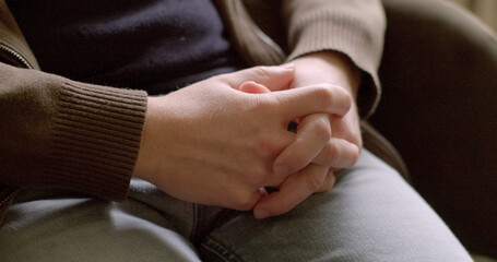 Close-up male hands. Close-up of interlocking fingers during person feeling insecure, anxious, or defensive. This gesture suggests that the individual is seeking comfort or reassurance. 