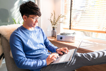 Asian man in casual clothes, typing on laptop about new business project and checking social media...