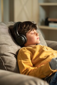 Relaxed young boy lying on the sofa enjoying music through headphones