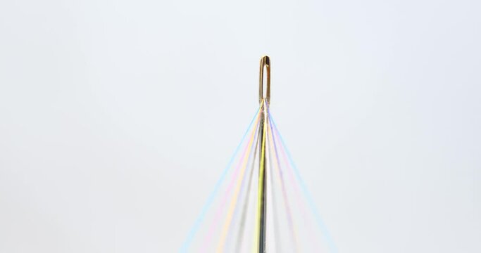 Rainbow Colored Threads Converge Through Needle Eyelet on a rotating table, white background