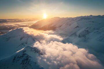 Aerial view of snow covered mountains with the sun rising above the clouds.