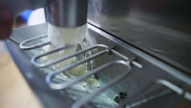 Closeup indoor shot of pasteurizer machine pouring ice cream into steel freezer. Ice cream manufacture concept. High quality 4k footage