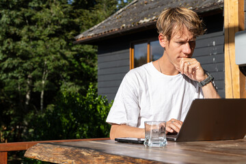 Young professional working remotely from a scenic vacation spot, laptop and phone in hand.