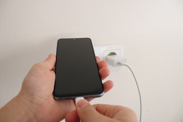 Hand holding a charging smartphone. Electrical outlet in the background. fast charging and...