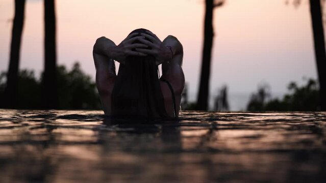 Girl in swimming pool on the seashore at sunset in