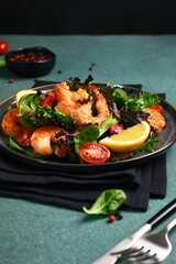 Salad with shrimp and tomatoes in a plate on a green background.