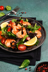 Salad with shrimp and tomatoes in a plate on a green background.