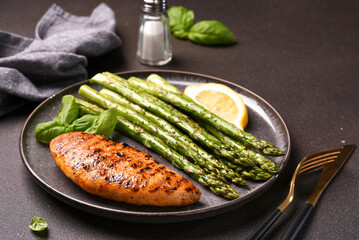 Baked asparagus and grilled chicken fillet in a plate on a dark background