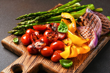 Grilled vegetables: asparagus,tomatos,onion on a wooden board on a black background