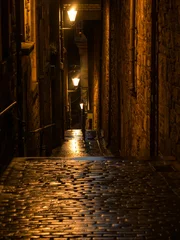 Cercles muraux Ruelle étroite A dark and narrow alley in a picturesque medieval town lit by street lanterns