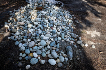 Large pile of round river rocks ready for spring gardening, outdoor public park on a sunny day
