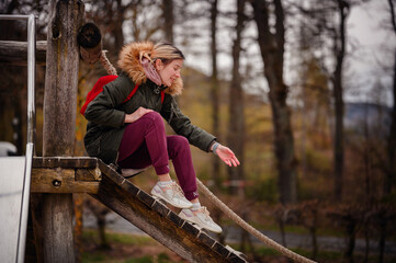 A woman sits contemplatively on a wooden beam at a playground, her casual pose and soft focus...