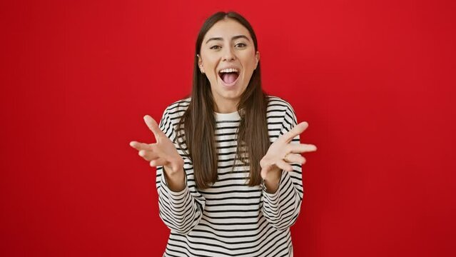 Overjoyed young hispanic woman in striped t-shirt raises arms for a warm hug on isolated red background. radiant smile lights up her beautiful face while standing ready to embrace happiness.