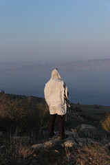 A Jewish man wraps himself in a tallit in prayer in nature