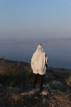 A Jewish man wraps himself in a tallit in prayer in nature