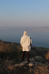 A Jewish man wraps himself in a tallit in prayer in nature