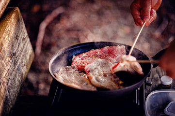 The rich scent of grilling steak fills the campsite as a camper flips the meat over a portable stove, showcasing outdoor culinary skills