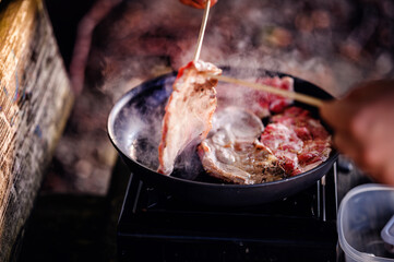 The rich scent of grilling steak fills the campsite as a camper flips the meat over a portable stove, showcasing outdoor culinary skills