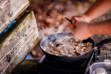 A camper meticulously seasons meat on a grill, demonstrating care and attention to detail in...